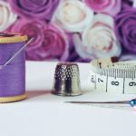 spool of purple thread near needle thimble and measuring tape